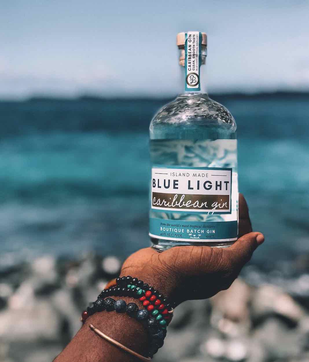 Hand holding a bottle of Blue Light Caribbean Gin against the ocean
